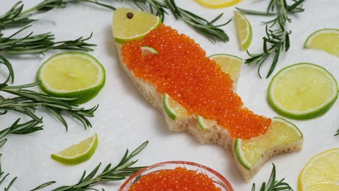 Sandwich with red caviar in shape of fish with lemon, rosemary rotate. Expensive healthy food concept. Sandwiches with salmon caviar salted roe.  Caviar on bread toast rotating close-up slow motion