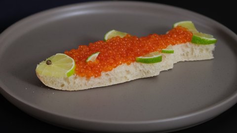 Sandwich with red caviar in shape of fish with lemon put on plate. Expensive healthy food concept close-up slow motion. Sandwiches bread or toast with salmon caviar salted roe. Fish dish. Sea food