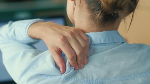 Back View of Woman Tired of Long Sedentary Lifestyle,Rubbing Massaging Neck.Female Experiencing Discomfort in a Result of Spine Trauma or Arthritis.Massaging and Stretching the Neck to Ease the Injury
