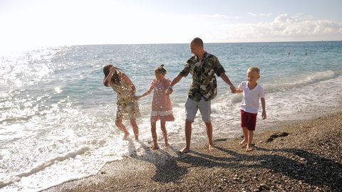 A happy family having fun with her children on the beach, they run along the shore, laugh and hug.