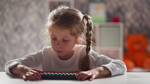 Tranquil little girl in white sweatshirt with colorful abacus solves tasks sitting at workplace during mathematics lesson close view slow motion