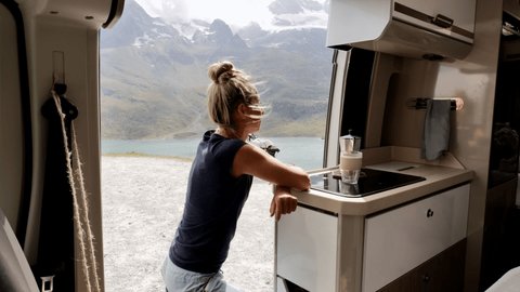 Young woman taking a moment to enjoy stunning natural landscape from her camper van. People living alternative lifestyle. 