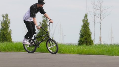 BMX Flatland bicycle rider performing a trick: Pedaling Time Machine No Hand. BMX Freestyle on Flatland. A young man doing a spinning trick on a bmx bike. 120 fps, ProRes 422, 10 bit video