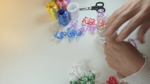 Timelapse. Making decorative ribbon arrange. Spools of colored plastic ribbon on white background. Old woman hands cutting and tying spiral decorative arranges for gift.