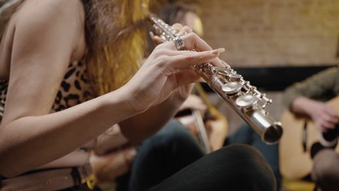 Close up shot of unrecognizable woman musician playing flute, enjoying rehearsal with music band, tracking shot, slow motion, free space