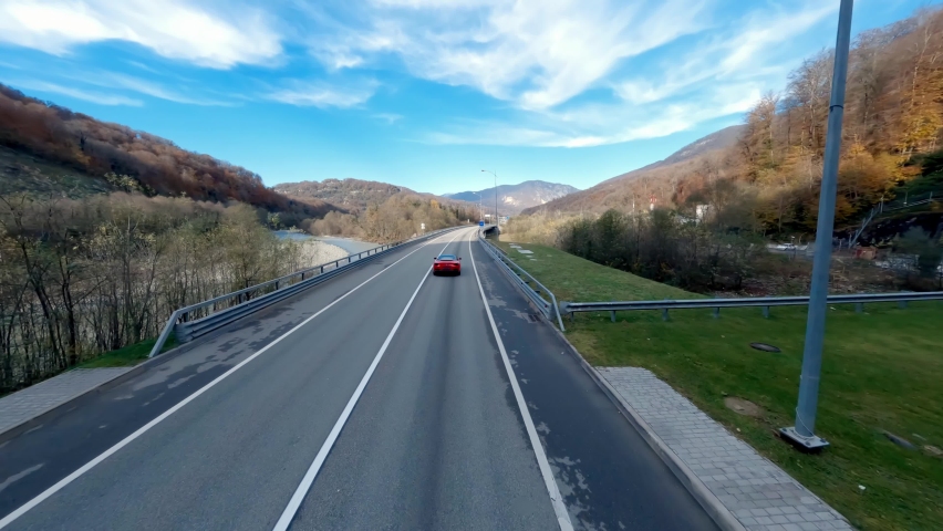 Luxury red sport car riding on street highway spring autumn nature landscape FPV drone aerial view. Premium automobile travel surrounded by forest river mountain area scenery and clear blue sky Royalty-Free Stock Footage #1089773313