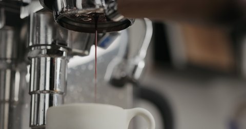 Slow motion low angle shot of espresso extraction from naked portafilter into white cup