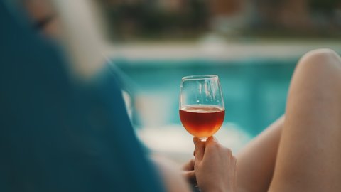 Woman with glass of wine is relaxing by the pool.
