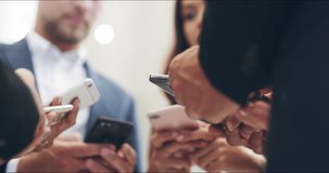 The age of technology has everyone typing. 4k video footage of a group of carefree young businesspeople standing in a circle while texting on their phones at work.