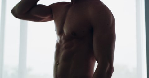 The ultimate in muscle definition. 4K video footage of a muscular man standing shirtless in his home.