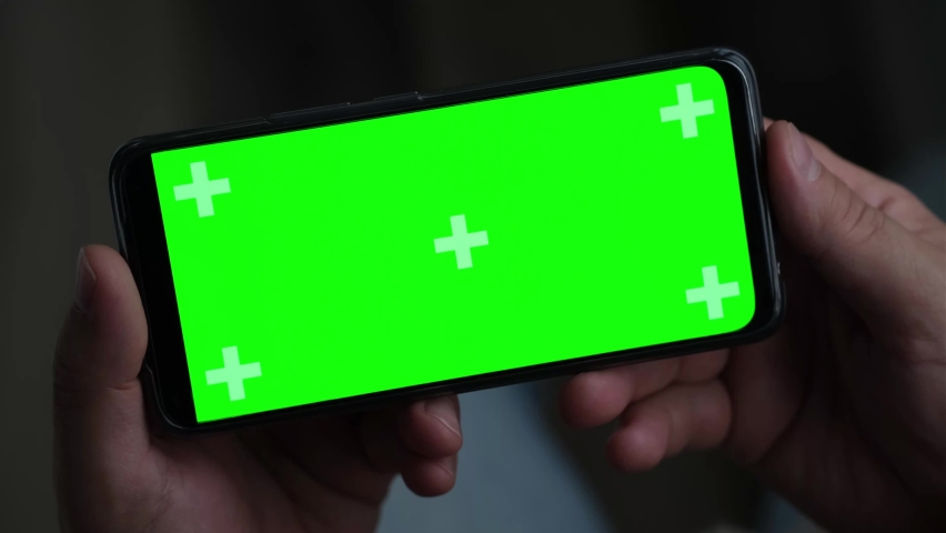 Closeup of man Hand is Holding Chroma Key Green Screen in horizontal Position without touching, swiping at night. Using Phone With Green Mock-up, Surfing Internet, Watching Content Videos, Apps. Royalty-Free Stock Footage #1089784025