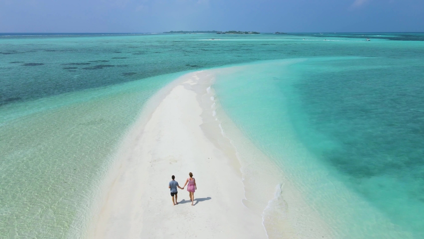 Couple walking together on beautiful beach with blue sea water and white sand. Sandbank at atoll island in Maldives. Love and honeymoon holiday vacation travel. Drone aerial video footage. 4k 60fps. Royalty-Free Stock Footage #1089786567