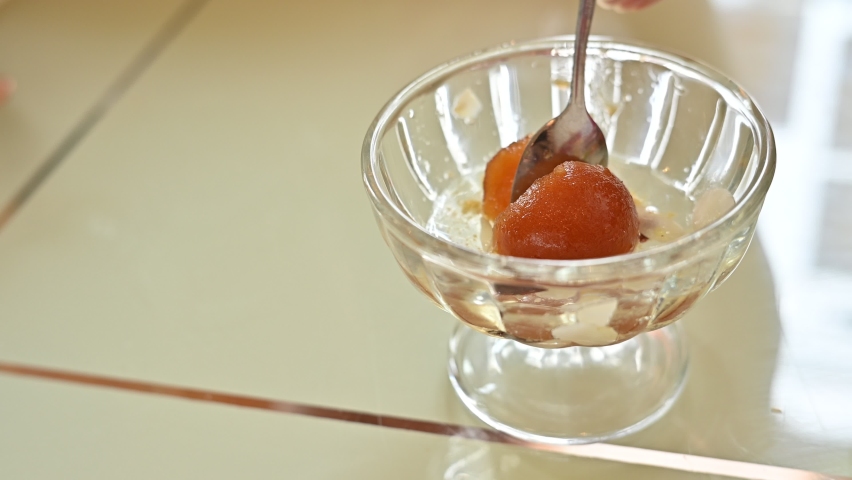Someone trying to eat Gulab jamun dessert by spoon. Gulab jamun is a classic Indian sweet.