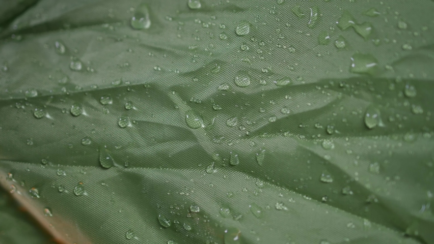 Water drops on a waterproof green polyester camping tent fabric with Gore-Tex membrane. Close-up slow motion macro with orange studio lighting. Royalty-Free Stock Footage #1089788677