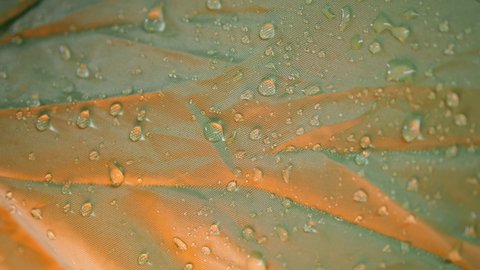 Water drops on a waterproof green polyester camping tent fabric with Gore-Tex membrane. Close-up slow motion macro with orange studio lighting.