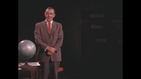 1950s: Man in suit and tie speaks. Man sits and crosses legs.