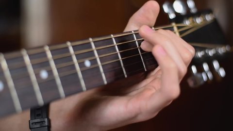Musician changing chords. Musician is playing music with chords on acoustic guitar. Man's playing acoustic guitar in the room.  Musician playing fingerstyle acoustic wooden guitar on a fretboard.