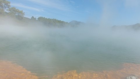 Camera rising and submersing into the clouds above hot steaming pond heated by geopthermal activity in Rotorua, New Zealand. Colorful and mystical scene. 