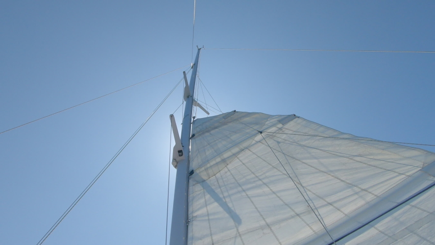 Raising the main sail of a sailing boat with the sun straight above the mast on a perfect blue sky  Royalty-Free Stock Footage #1089792785