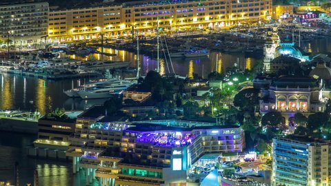 Aerial top view of Monaco from the grand corniche road night timelapse, Monaco France. Evening illumination. Traffic on the road. Reflections in water of harbor with yachts