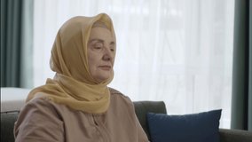 Senior woman in turban sitting alone at home or nursing home. The concept of being alone, aging alone.Close up and slow motion video.