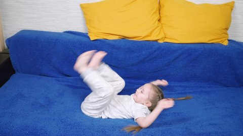 Acrobatic exercises kid, childhood. Family. Kid does somersaults, rolls over. Child girl plays in room, does somersaults on sofa in room. Little girl have fun doing somersault at home, sports game.
