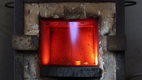 Blacksmith forge hot oven with hot flame. Smith heating iron piece of steel in fire of red-hot forge