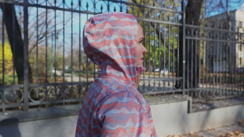 A girl in a hoodie walks along a metal fence.