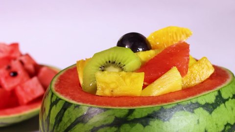 Watermelon bowl filled with fresh cut fruits and cut watermelon rotating