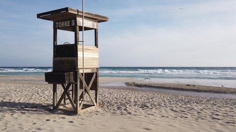 Static shot of a lifeguard tower on the beautiful beach of Son Bou, Menorca. Empty beach and sea with waves.