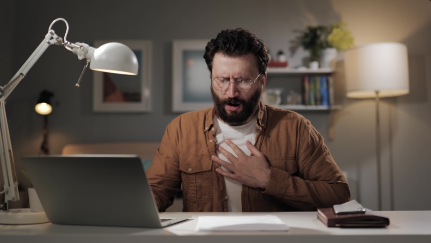 Breathing problems. Bearded middle-aged man at computer with panic attack. Computer user with respiratory issues having trouble breathing and holding hand on chest | Shutterstock HD Video #1089804855