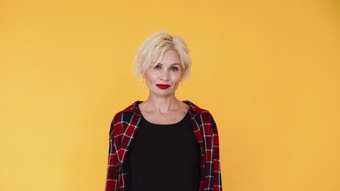 Feminine power. Beautiful woman. Stylish look. Smiling confident middle-aged lady blonde hairstyle red lipstick chattered casual shirt isolated yellow.