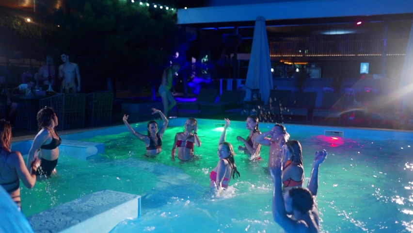 Friends have night pool party in a private villa swimming pool. Cheerful young people in swimwear splashing water, dancing and partying in luxury resort. Happy men and women hanging out. Slow motion. | Shutterstock HD Video #1089810425