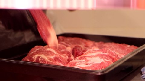 Close-up of salesman lays out the red raw meat into the pallet for window display in grocery department at supermarket, 4k footage