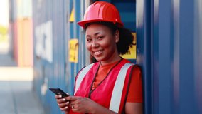 Black woman look at camera and smile. working by smartphone. Black female dock worker control loading containers box from cargo at warehouse container yard. - Powered by Shutterstock - Get 15% off with code: PIKWIZARD15