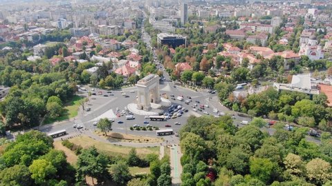 Aerial video drone of Arc de Triomphe in Bucharest from above, arc de triumf in romania, parc view from above with cars driving by on a sunny summer day with green trees