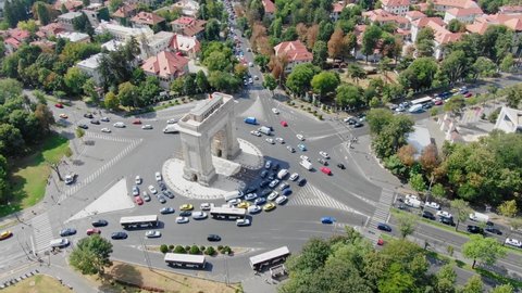 overhead aerial video of Arc de Triomphe in Bucharest from above, arc de triumf in romania, parc drone view from above with cars driving by on a sunny summer day with green trees dolly zoom