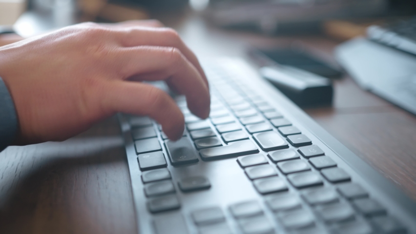 Man with a Blue Shirt, is working on a computer with a Gray Keyboard and a wooden Desk
