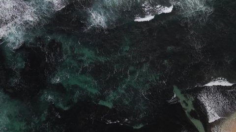 A bird's eye view footage of the open waters with various waves and sea foam. The aerial footage starts shooting on the grounding upwards towards the open sea to the horizon. Lots of seagrass