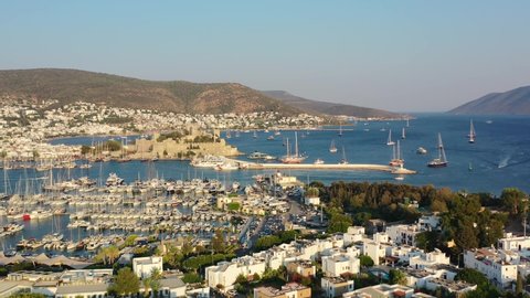 aerial drone revealing the coastal town of Bodrum with a castle and marina full of sailboats in the Aegean Sea of Mugla Turkey on a summer afternoon during sunset