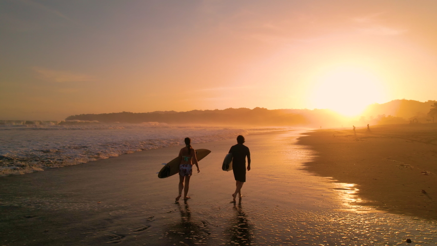AERIAL SILHOUETTE: Two surfers carrying surfboards and checking waves after surf session. Surf friends walking on the beach in golden light. Gorgeous summer scenery at Playa Venao in Panama. - Powered by Shutterstock - Get 15% off with code: PIKWIZARD15