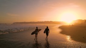 AERIAL SILHOUETTE: Two surfers carrying surfboards and checking waves after surf session. Surf friends walking on the beach in golden light. Gorgeous summer scenery at Playa Venao in Panama. - Powered by Shutterstock - Get 15% off with code: PIKWIZARD15