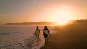 AERIAL SILHOUETTE: Couple of surfers walking down the beach carrying surfboards. Surf friends checking waves in golden light after surf session at sunset. Gorgeous scenery at Playa Venao in Panama. - Powered by Shutterstock - Get 15% off with code: PIKWIZARD15