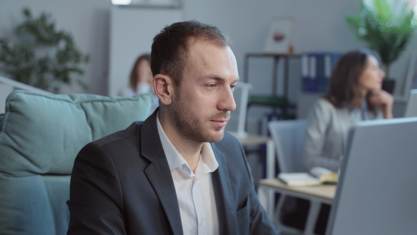 Close-up shooting of smiling successful manager of company sitting at new computer in modern comfortable office. Portrait of confident attractive young man in black suit looking directly at camera Royalty-Free Stock Footage #1089814191