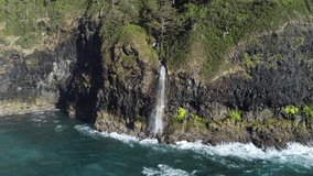 Aerial shot of a Waterfall off of Cape Lookout, Oregon dropping into the surf with slight hint of a rainbow.  As video backs away, much of the cape, ,forests and the Coast Range come into view.