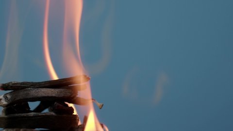 The wooden fire is orange, and the smoke of the fire from the mustard tree is on a red background. Close-up of a flame with white smoke. Slow motion, 4K.