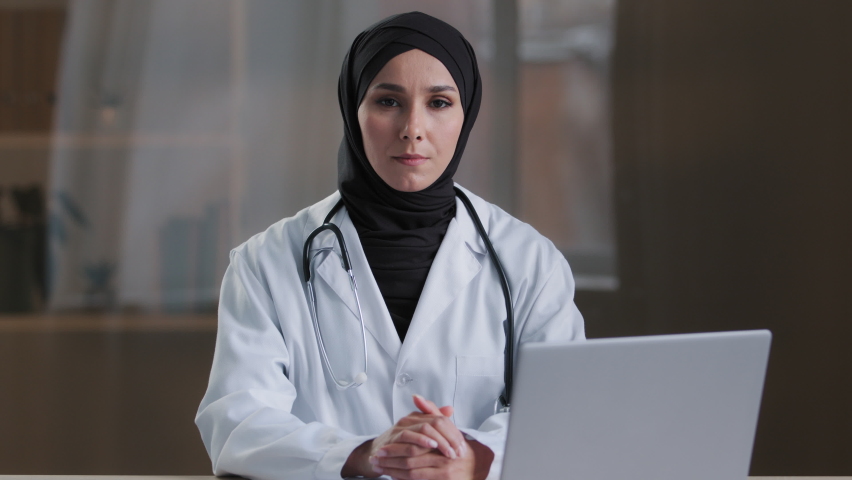 Happy smiling arabian nurse islamic doctor therapist wear white medical coat hijab sitting at clinic muslim female practitioner intern posing crossed arms looking at camera medical healthcare service Royalty-Free Stock Footage #1089818181