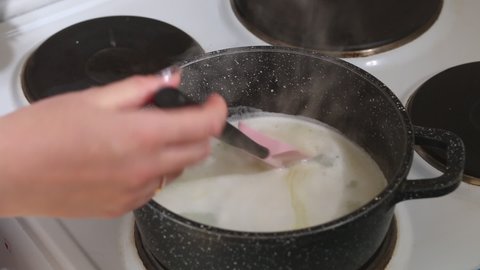 A woman adds flour to a saucepan. Preparing choux pastry for eclairs. Close-up.