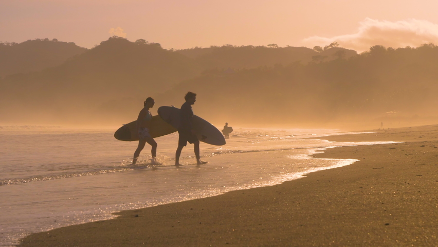 SLOW MOTION: Couple of surfers coming out of water after sunset surf session. Two friends after surf session in golden light at Playa Venao surf spot. Beach lifestyle shot in gorgeous light. | Shutterstock HD Video #1089823755