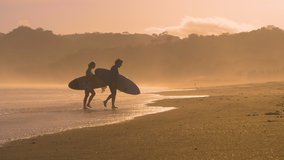 SLOW MOTION: Couple of surfers coming out of water after sunset surf session. Two friends after surf session in golden light at Playa Venao surf spot. Beach lifestyle shot in gorgeous light. - Powered by Shutterstock - Get 15% off with code: PIKWIZARD15